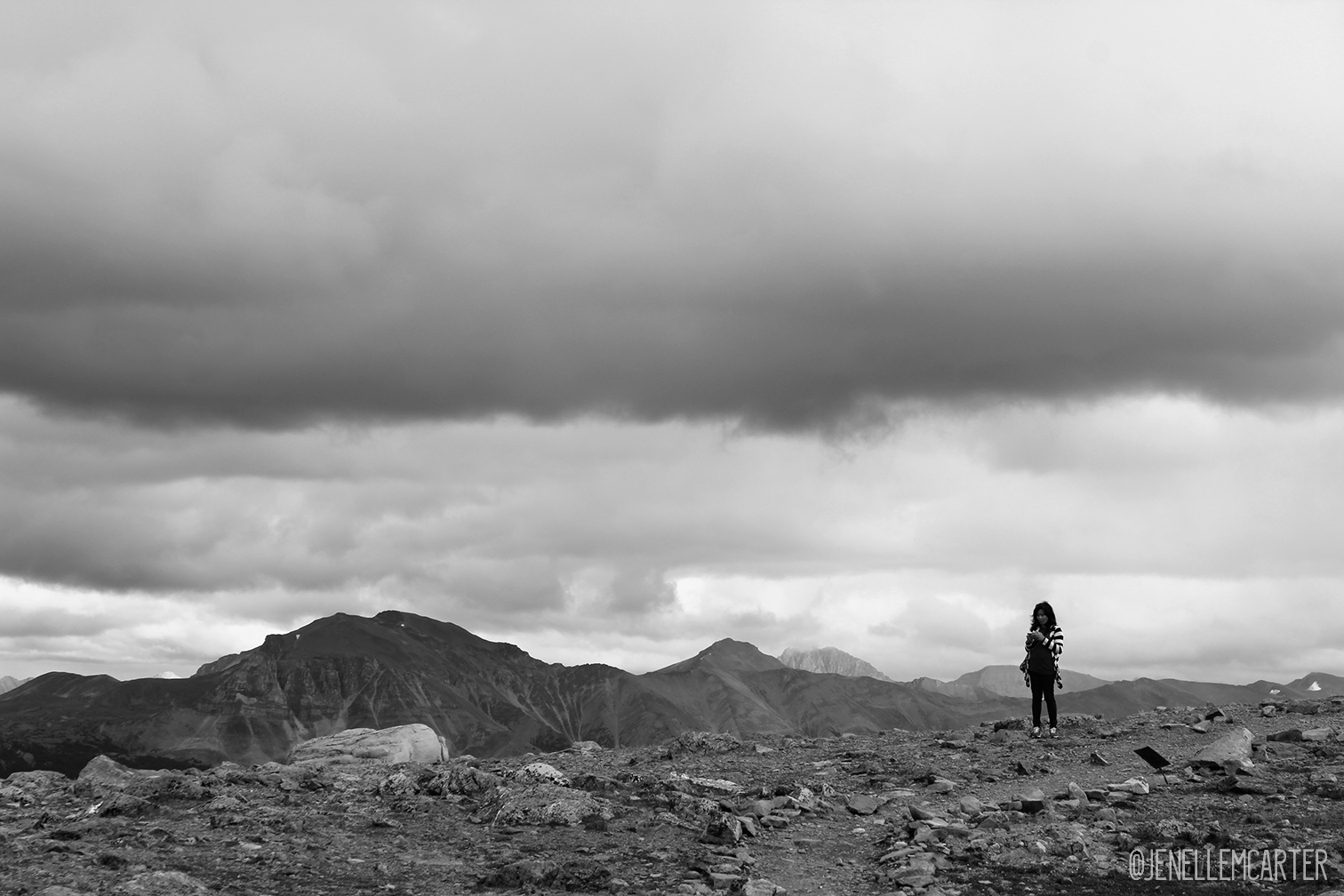 A woman stands alone on top of a mountain.