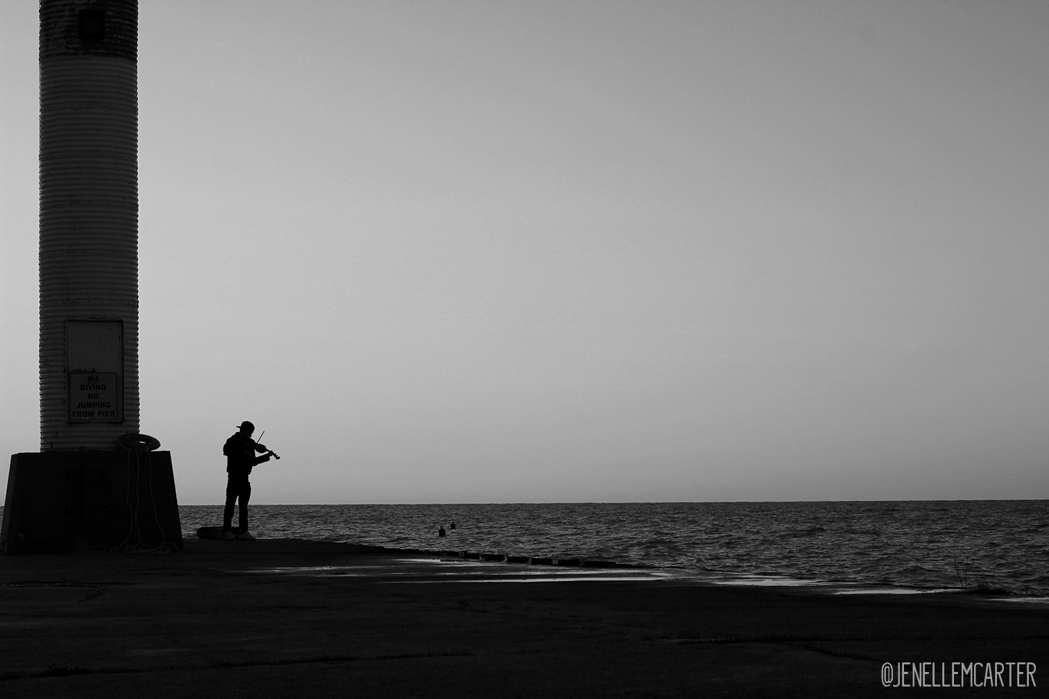 The silhouette of a young man playing the violin on a pier.