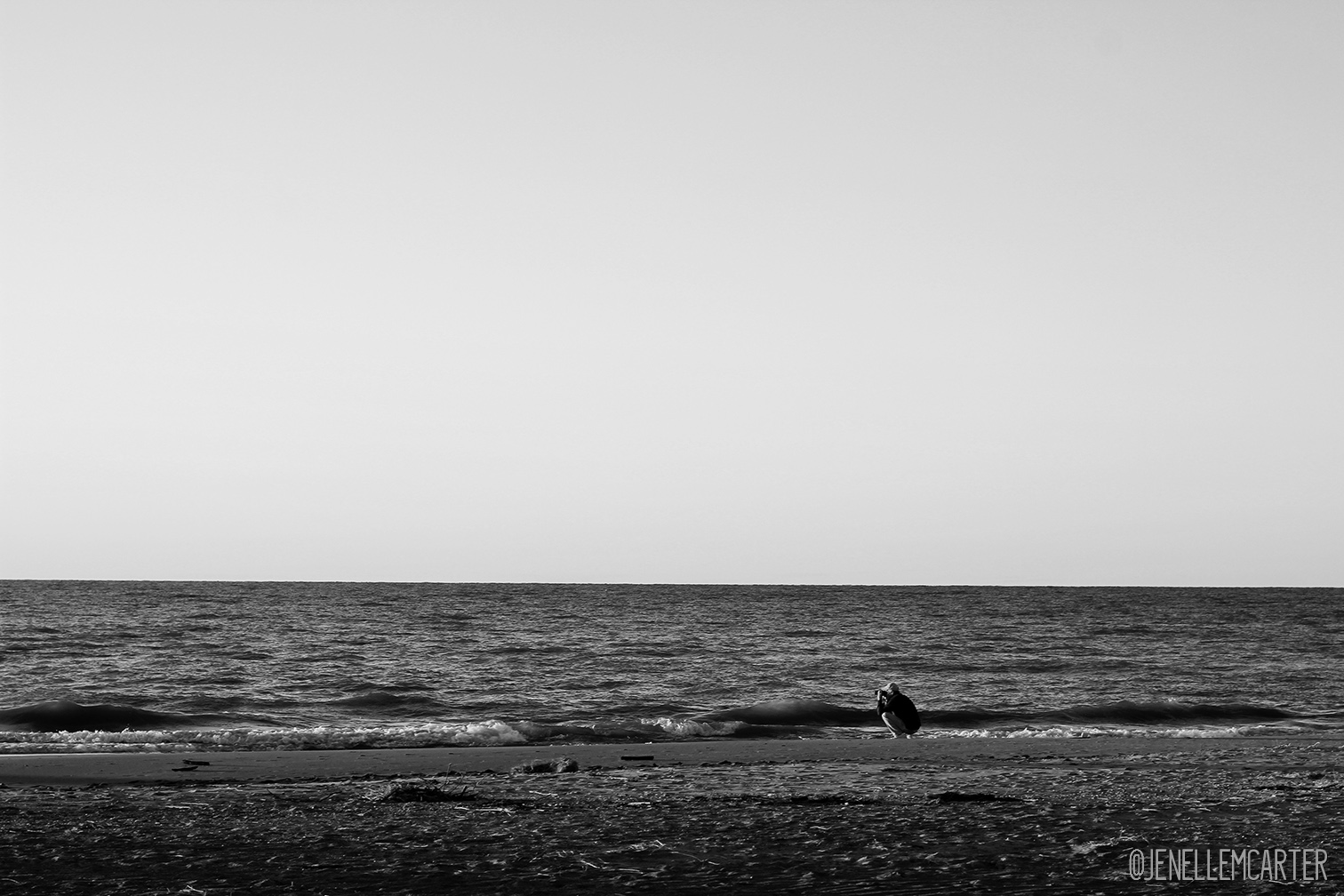 A man squats down to take a photograph on the beach.