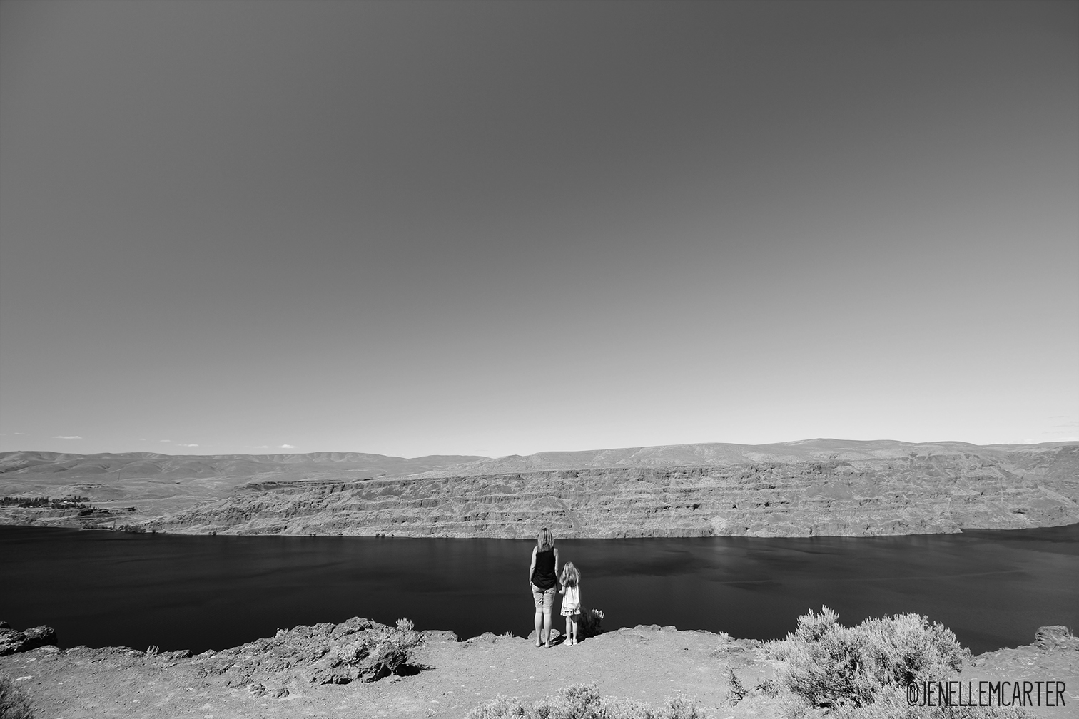 A mother and daughter stand alone looking out over a scenic landscape.